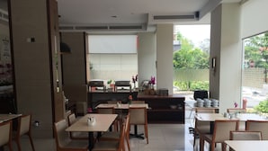 A restaurant with multiple tables and chairs, a kitchen area with grills, and a view of greenery outside. - C'haya Hotel (Kota Kinabalu)