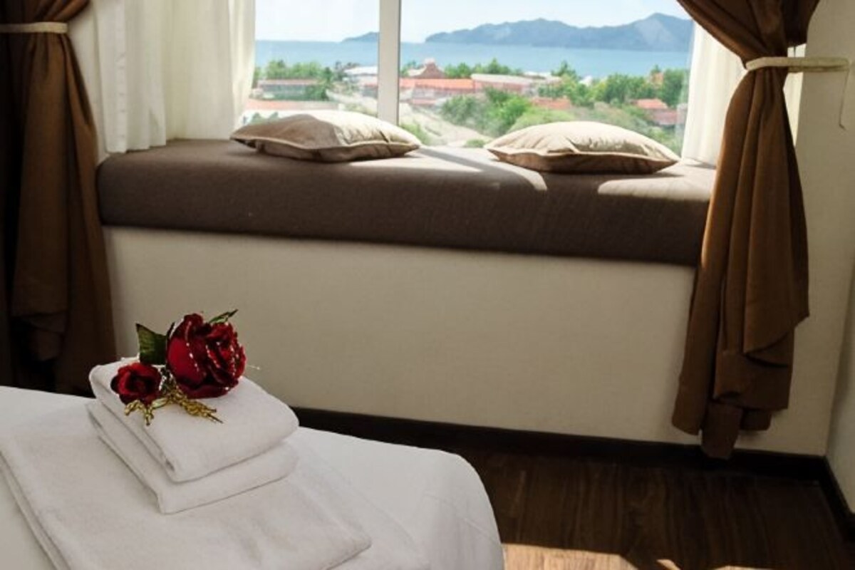 A room with a bed, a window with a view, and a decorative item on the bed.