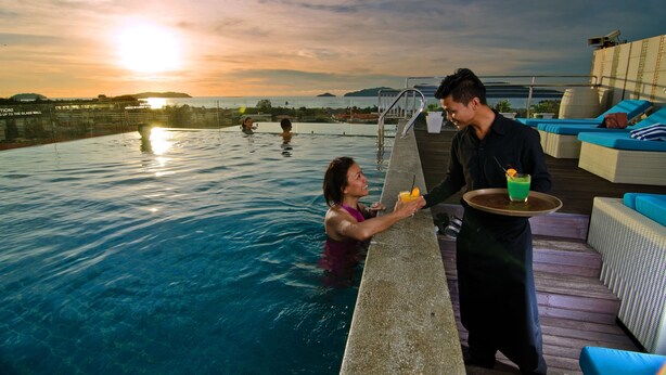 A poolside area with a clear view of the sunset over the water, a lounge area with blue cushions, and a person serving a drink. - C'haya Hotel (Kota Kinabalu)