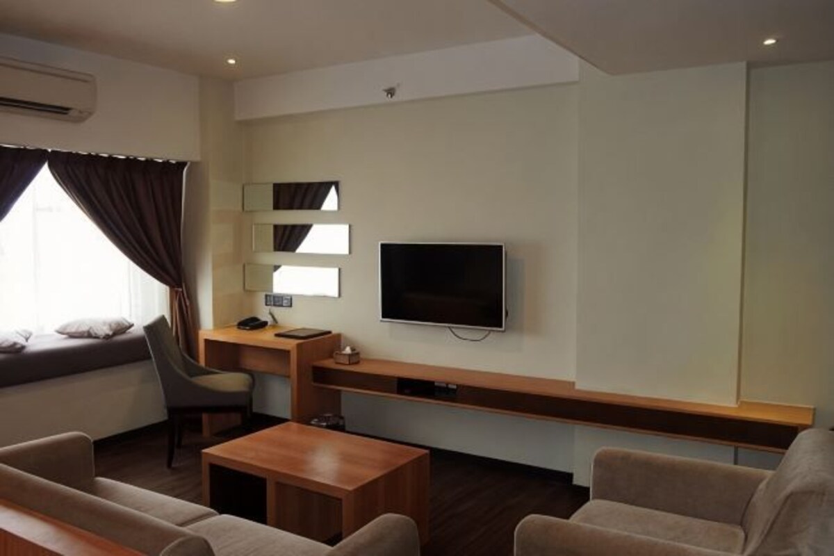 A modern hotel room with a flat-screen TV, a sofa, a desk, and a chair.