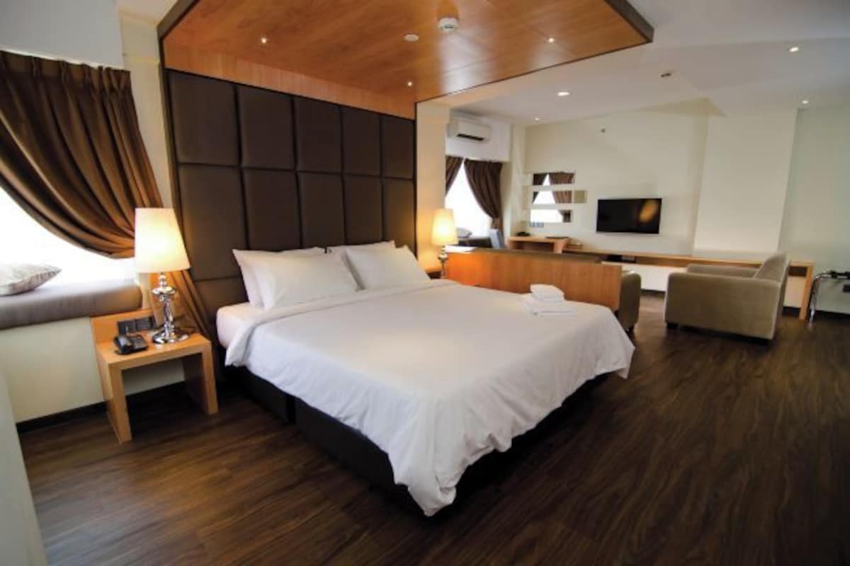 Una habitación de hotel moderna con una cama grande, un cabecero de madera, un televisor, un sofá y un escritorio.