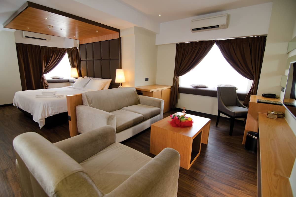 A hotel room with two beds, a sofa, a small table with a flower arrangement, a chair, and a desk with a telephone.