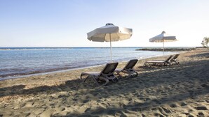 A beach with two lounge chairs and two umbrellas. - Harmony Bay Hotel (Limassol)