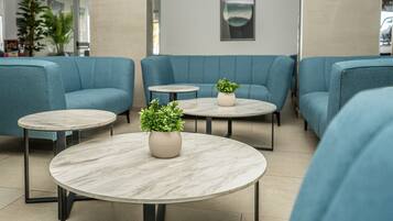 A modern lounge area with blue sofas and round marble tables, each with a potted plant.
