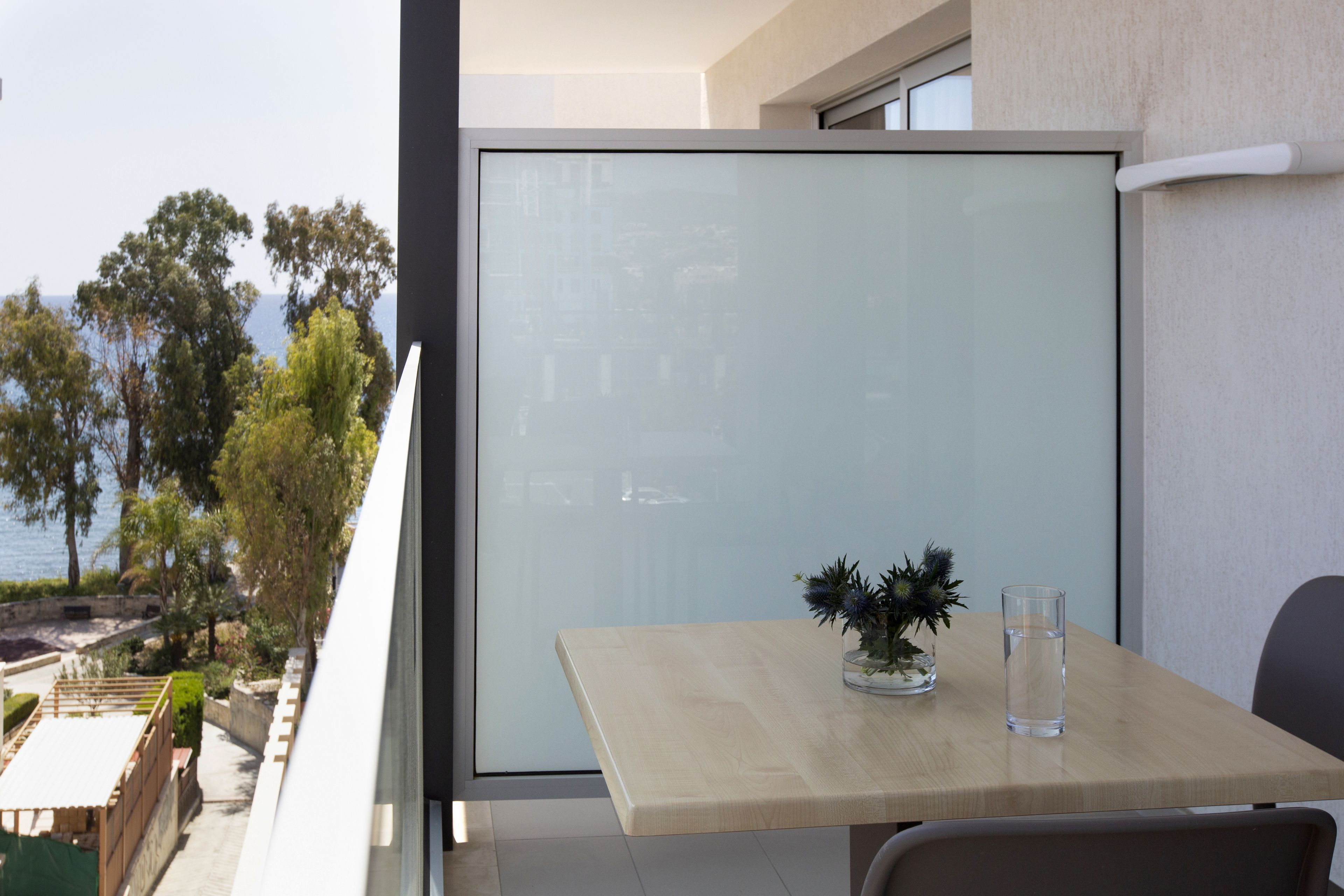 A balcony with a table, a chair, a glass of water, and a potted plant.