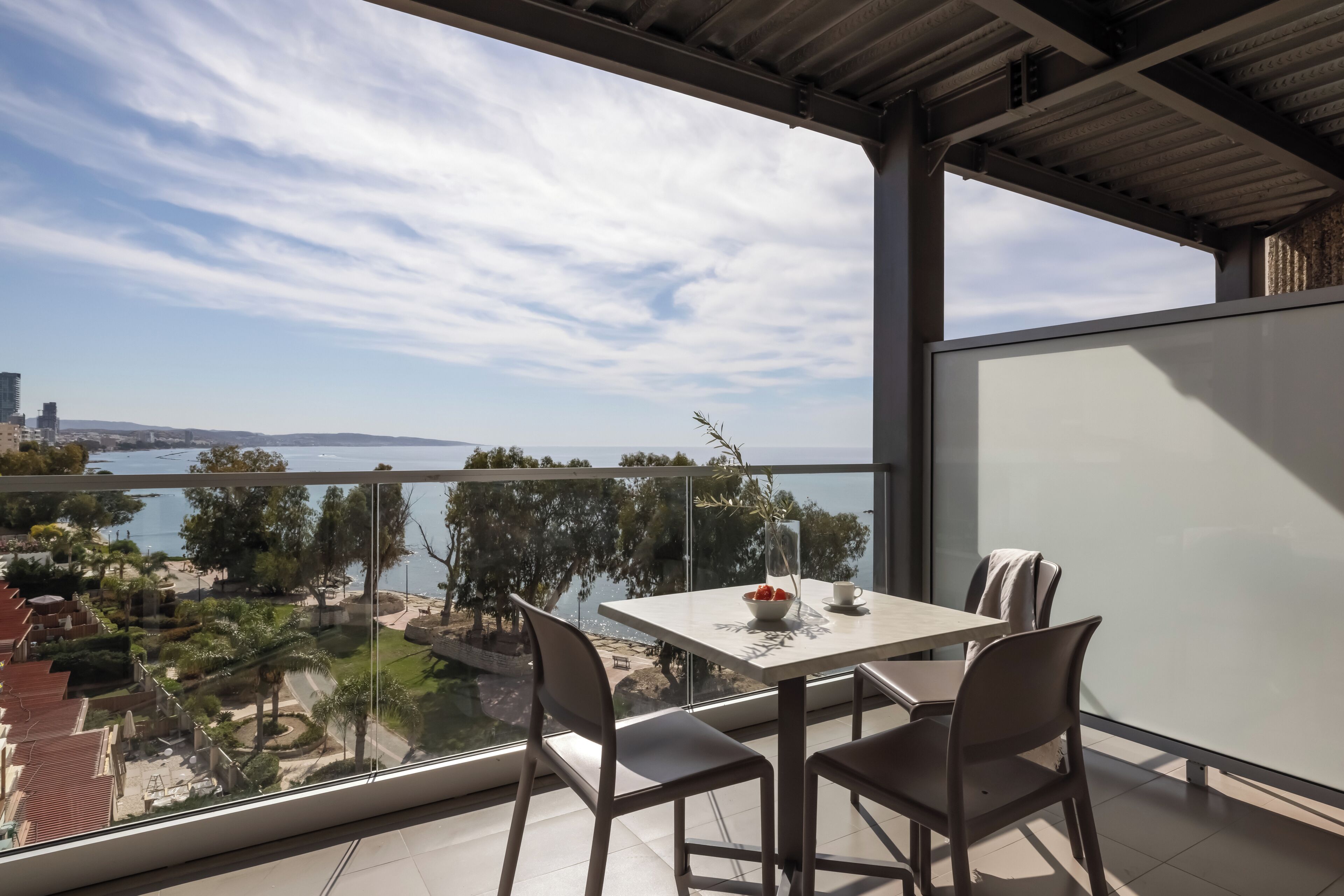 A balcony with a table and chairs, overlooking a body of water and a cityscape.