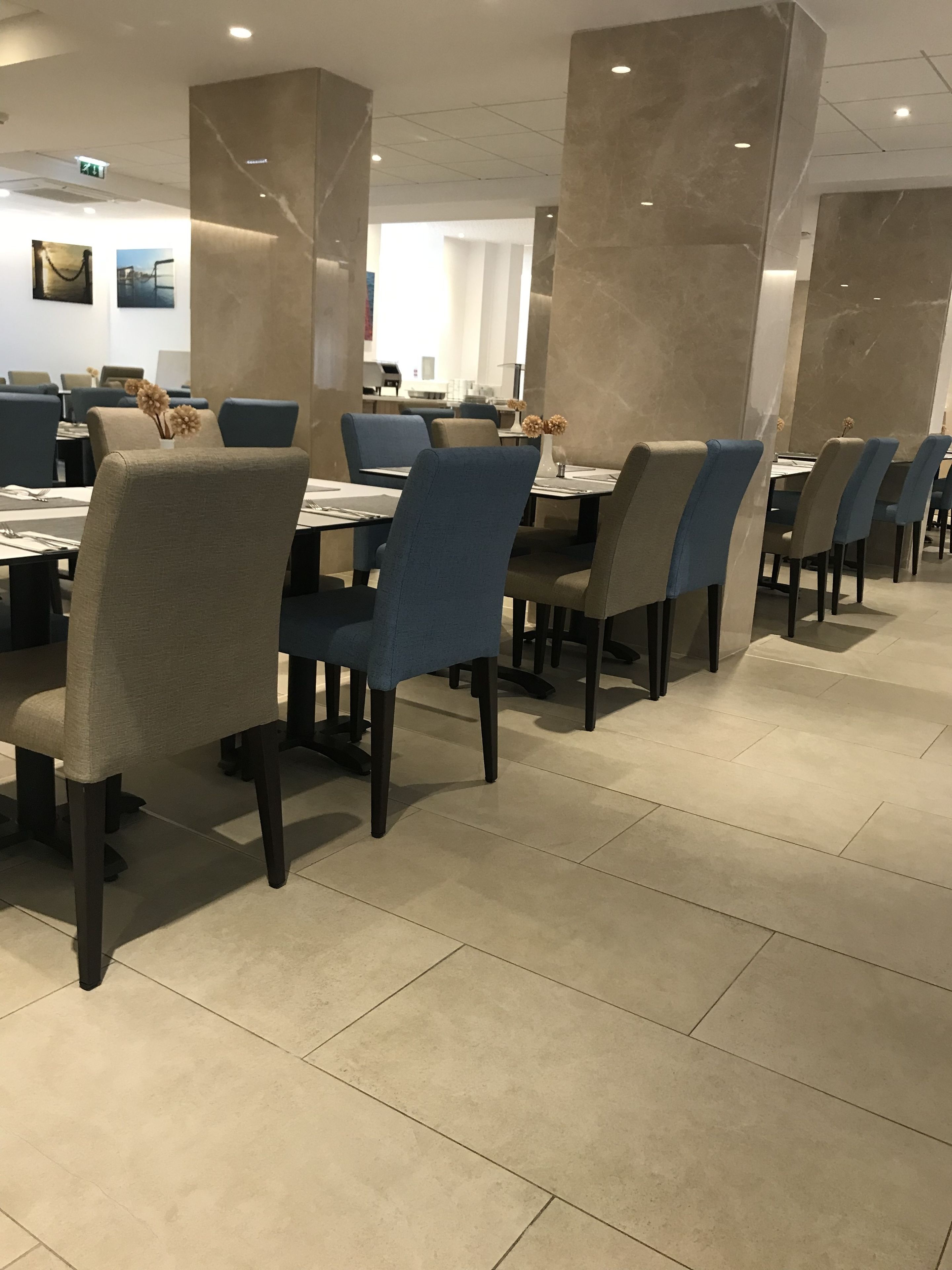 Un espace de restauration moderne avec des chaises bleues et beiges, des piliers en marbre et un sol carrelé.