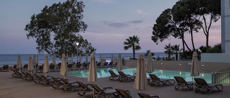 A poolside area with lounge chairs and umbrellas, overlooking the ocean.