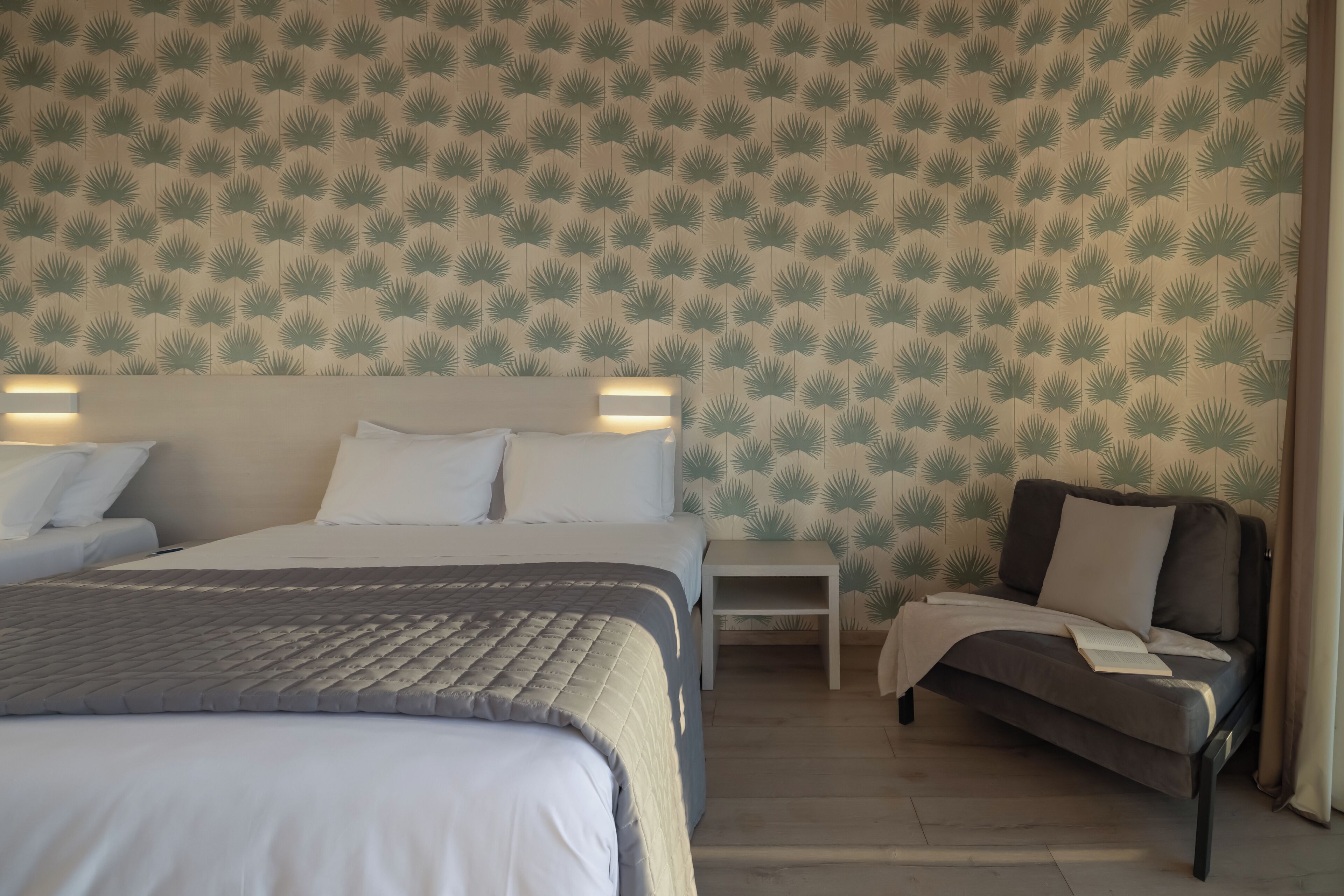 Habitación de hotel con cama, sofá, mesita de noche y pared con diseño de hojas.