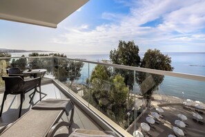 A balcony with a glass railing overlooking a beach and sea, furnished with chairs and a table. - Harmony Bay Hotel (Limassol)