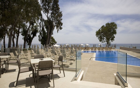 A poolside area with lounge chairs and umbrellas, overlooking a body of water. - Harmony Bay Hotel (Limassol)