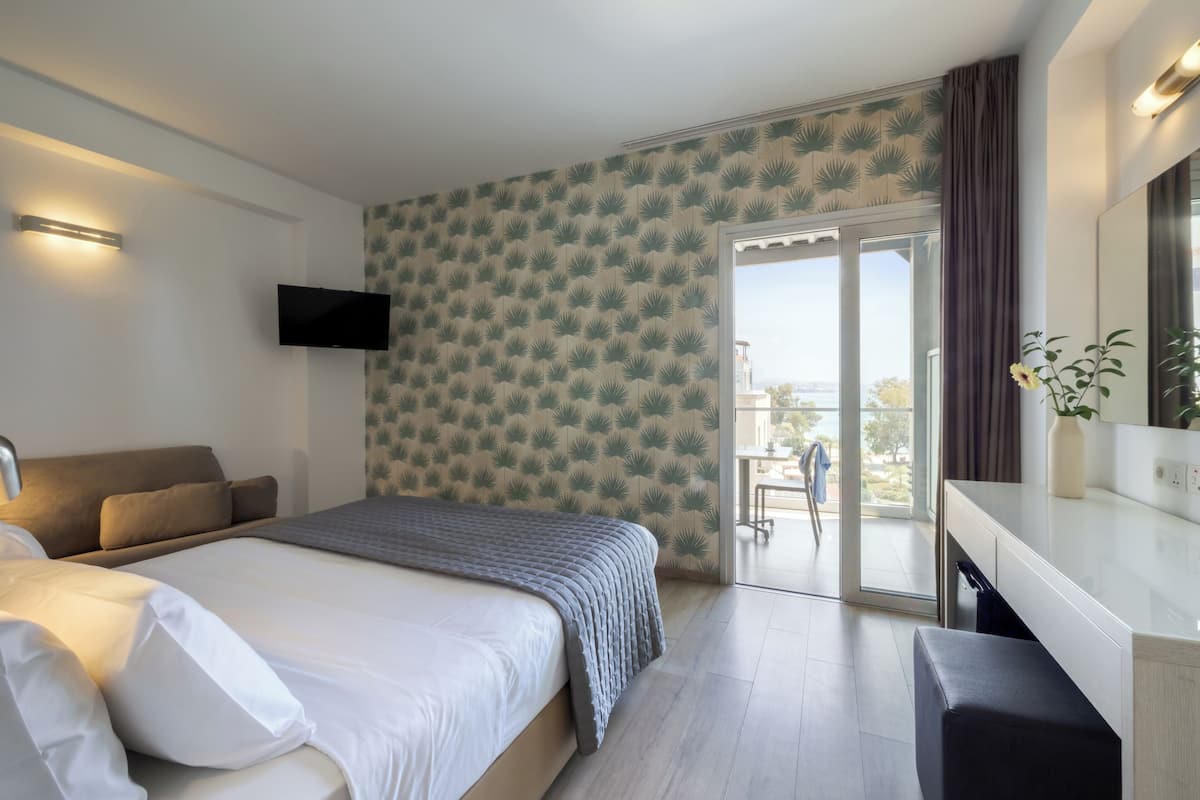 A bedroom with a bed, a TV, a desk, and a view through a glass door.