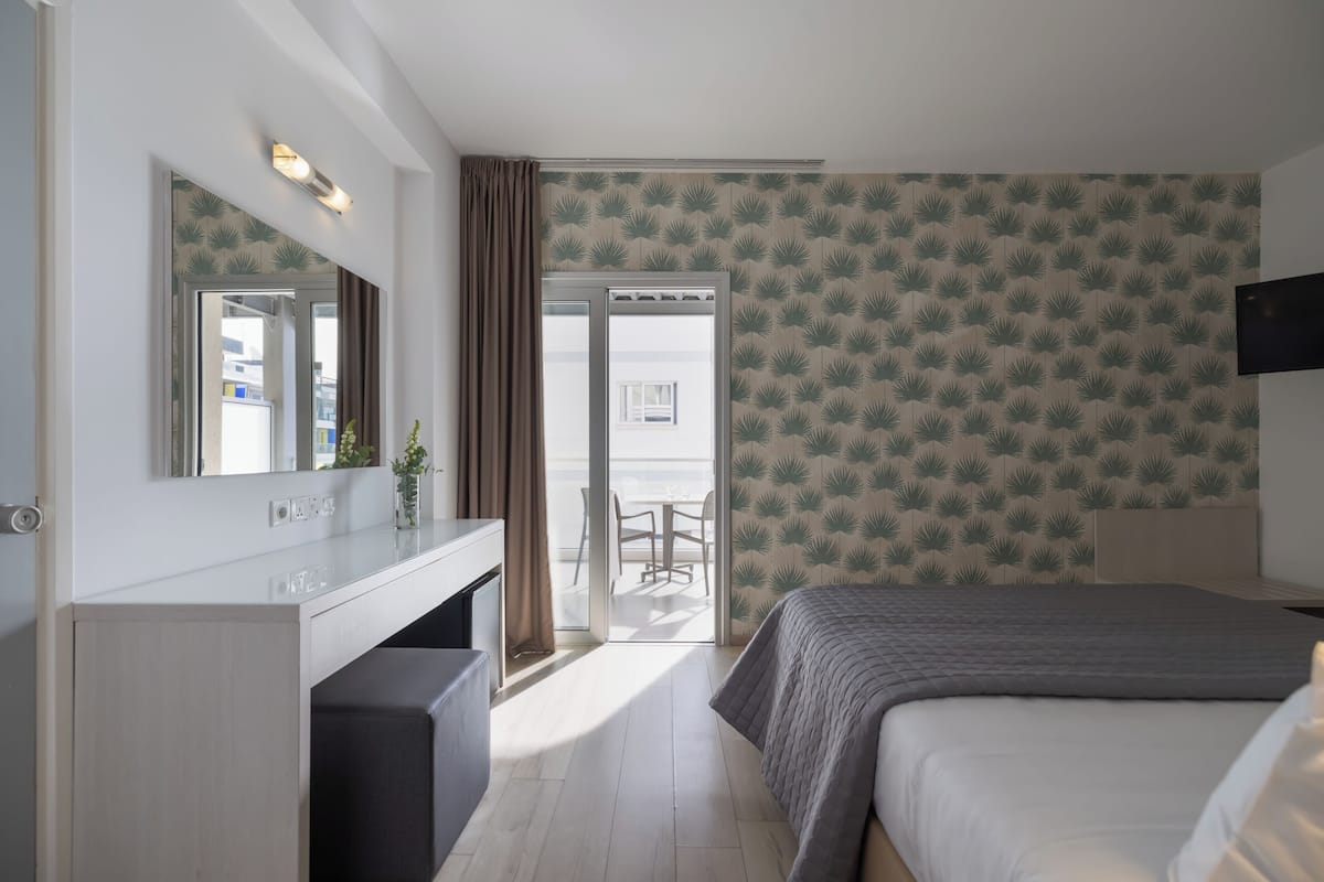 A hotel room with a bed, a desk, a mirror, a TV, and a balcony with a view.