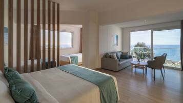 Une chambre d’hôtel avec un grand lit, un canapé, une table à manger et un balcon avec vue sur la mer.