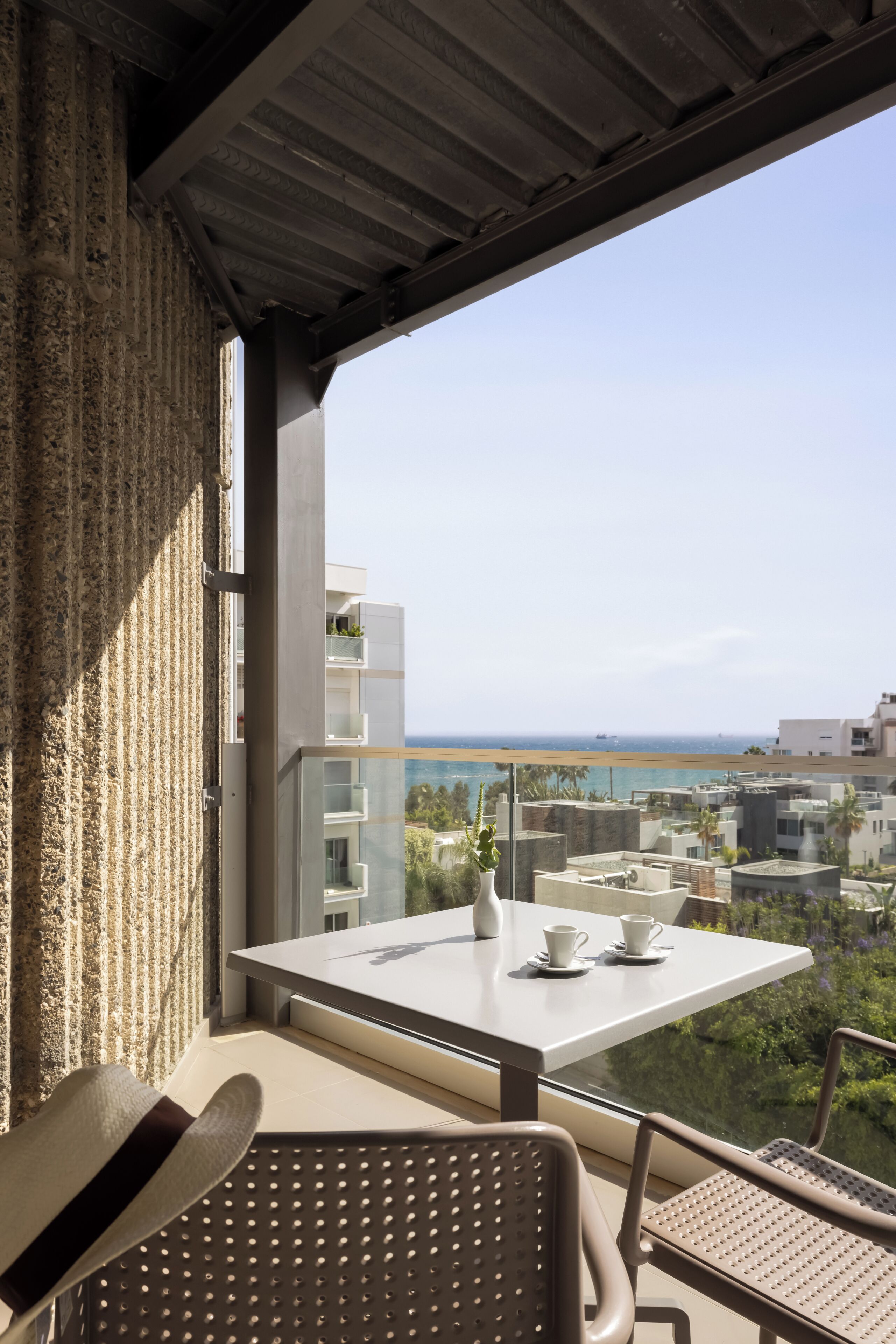A balcony with a table and chairs, a view of the ocean, and buildings in the background.