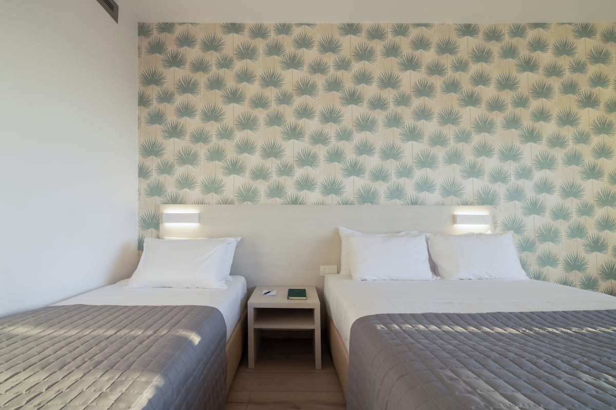 A hotel room with two beds, a nightstand, and a wall with a leaf pattern.