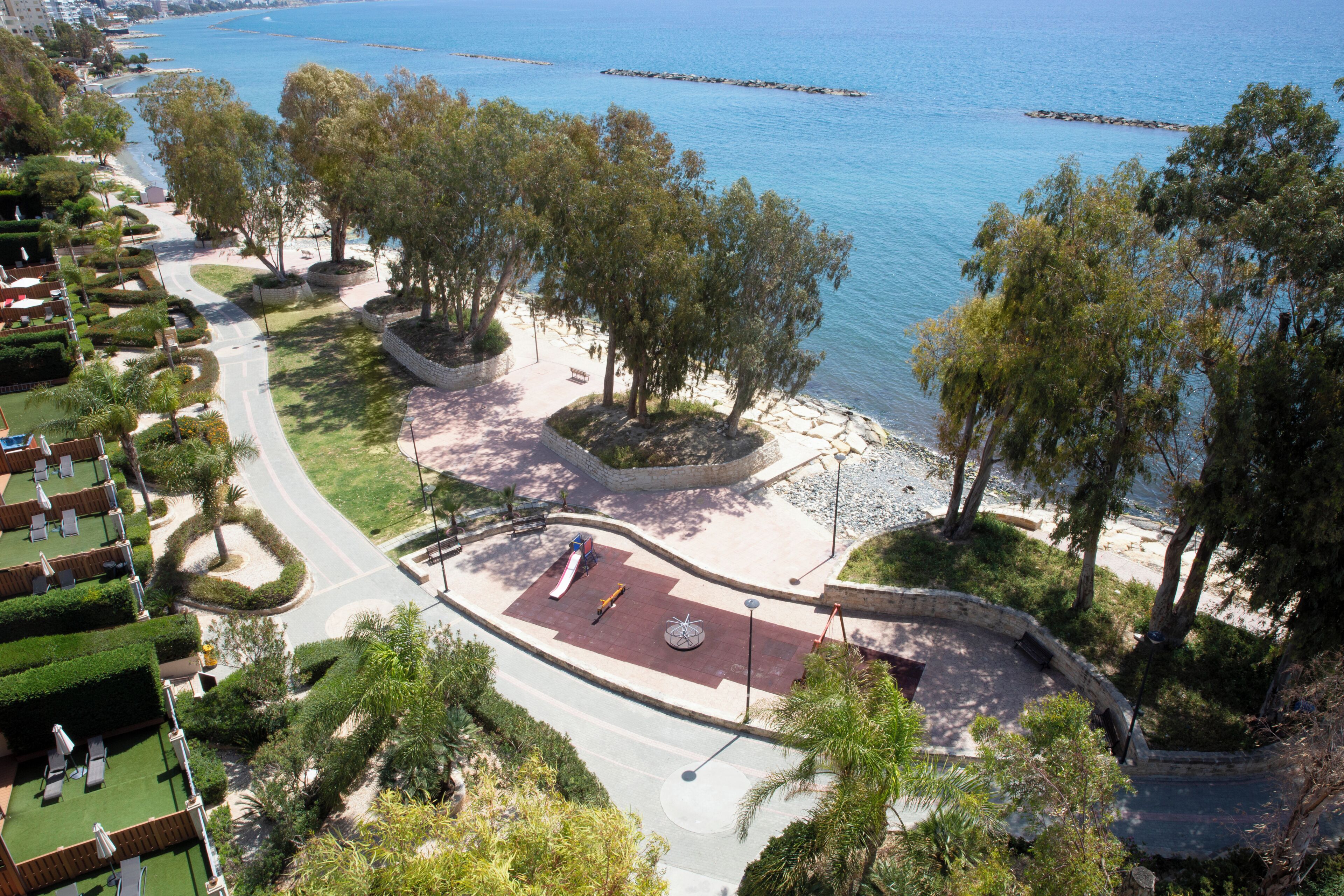 A coastal hotel with a paved walkway, landscaped areas, and a view of the sea.