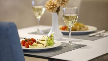 A dining table with plates of food, glasses of white wine, and a vase with flowers.