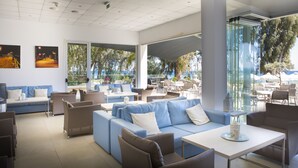 A modern outdoor seating area with blue sofas and white tables, overlooking a pool and outdoor dining area. - Harmony Bay Hotel (Limassol)
