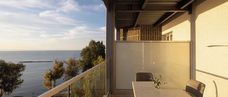 Een balkon met een tafel en stoelen, met uitzicht op een waterpartij en bomen.