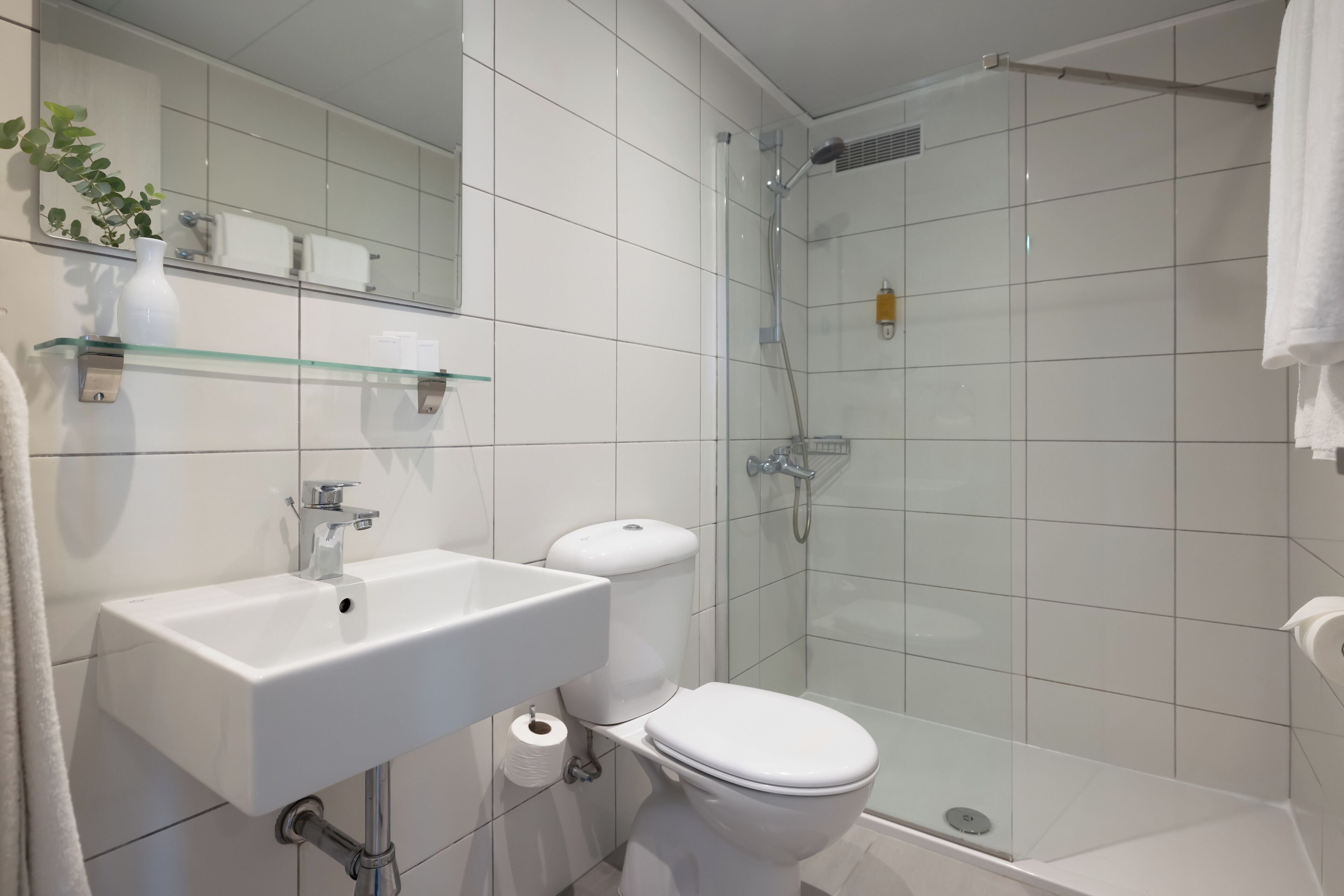 Un baño moderno con cabina de ducha de vidrio, un lavabo blanco y un inodoro.