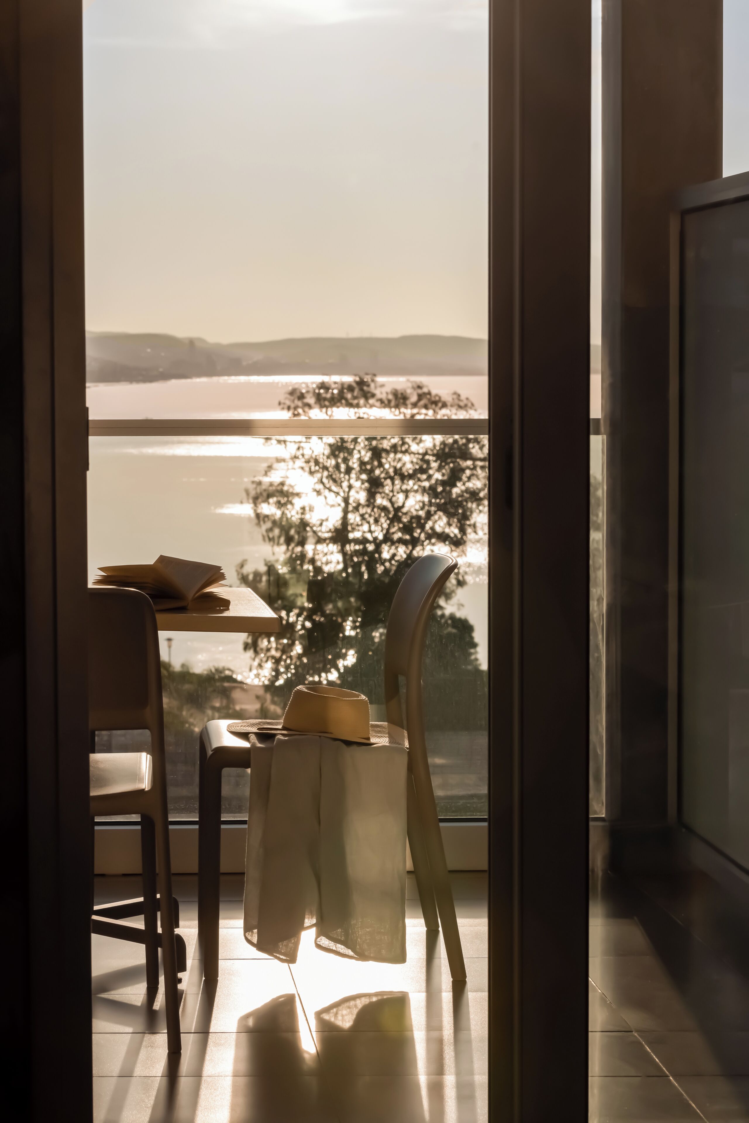 A room with a view of a body of water, a table with a book, and a chair.