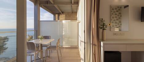 A modern room with a balcony, a dining area, a bed, a desk, and a mirror.