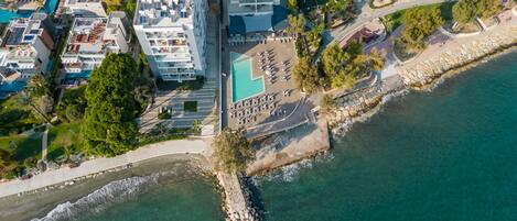 Vista aérea de un hotel costero con varias construcciones, una playa y un litoral rocoso.