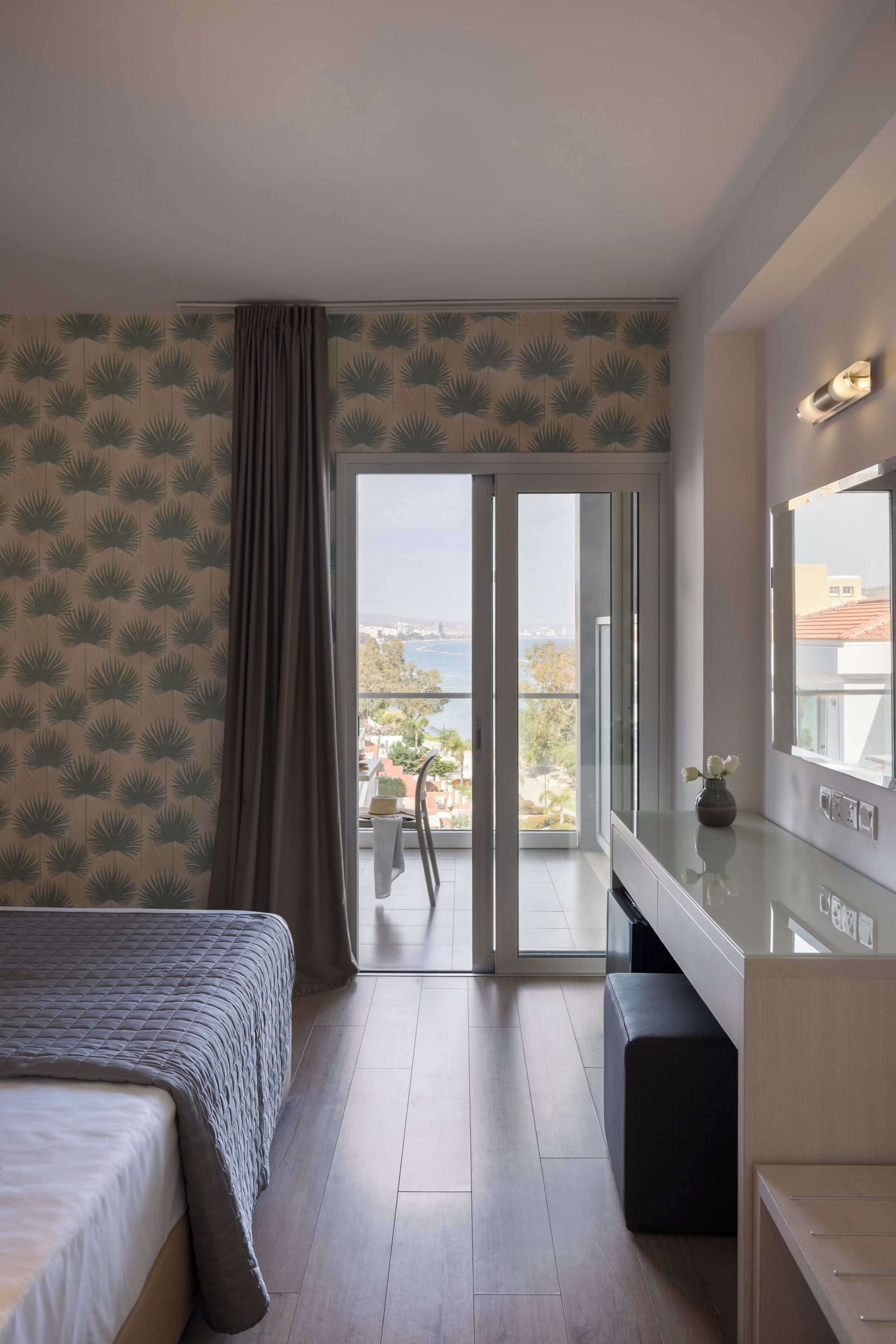 A modern hotel room with a bed, a desk, a chair, and a balcony with a view.