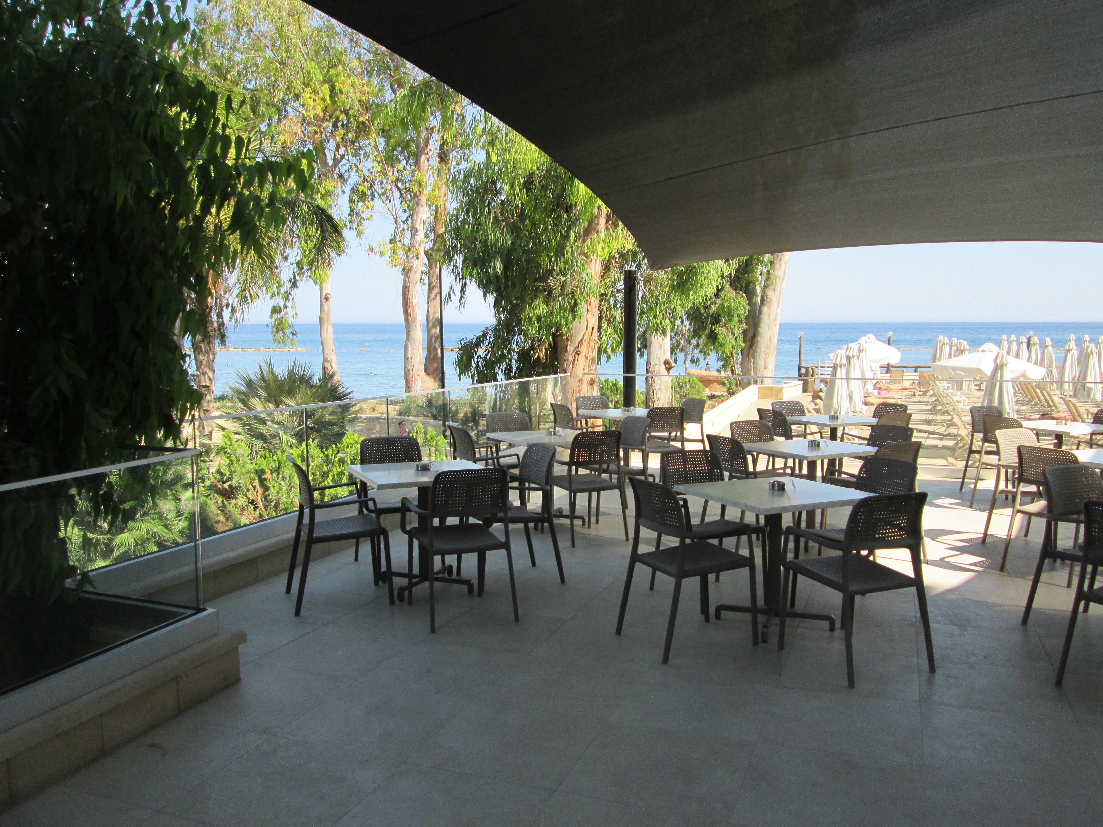 An outdoor dining area with tables and chairs, overlooking a beach and the sea.