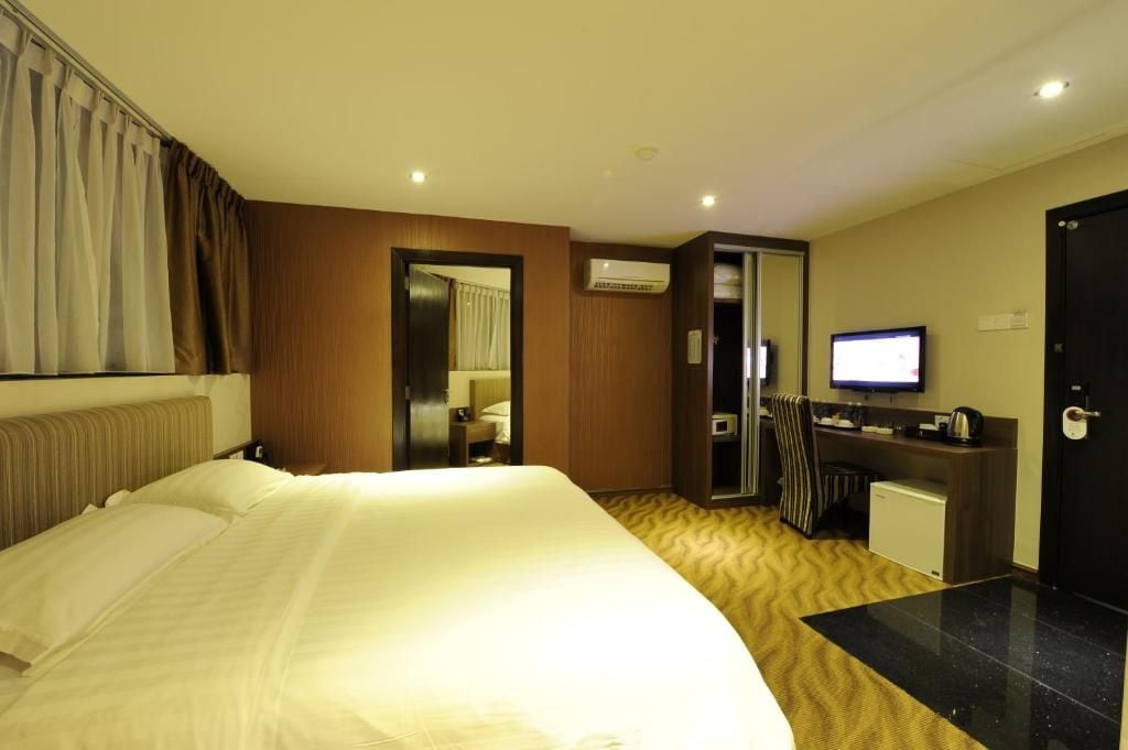 A hotel room with a large bed, a desk with a computer, a television, and an air conditioning unit.