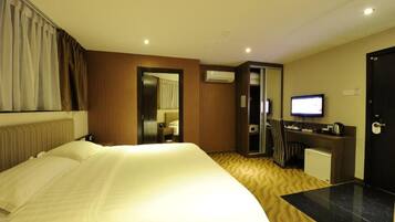 A hotel room with a large bed, a desk with a computer, a television, and an air conditioning unit.