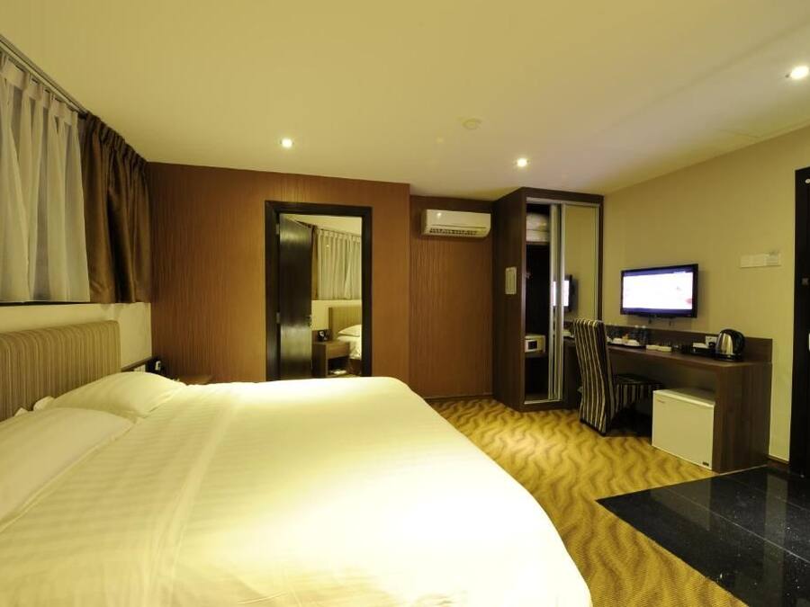 A hotel room with a large bed, a desk with a computer, a television, and an air conditioning unit.