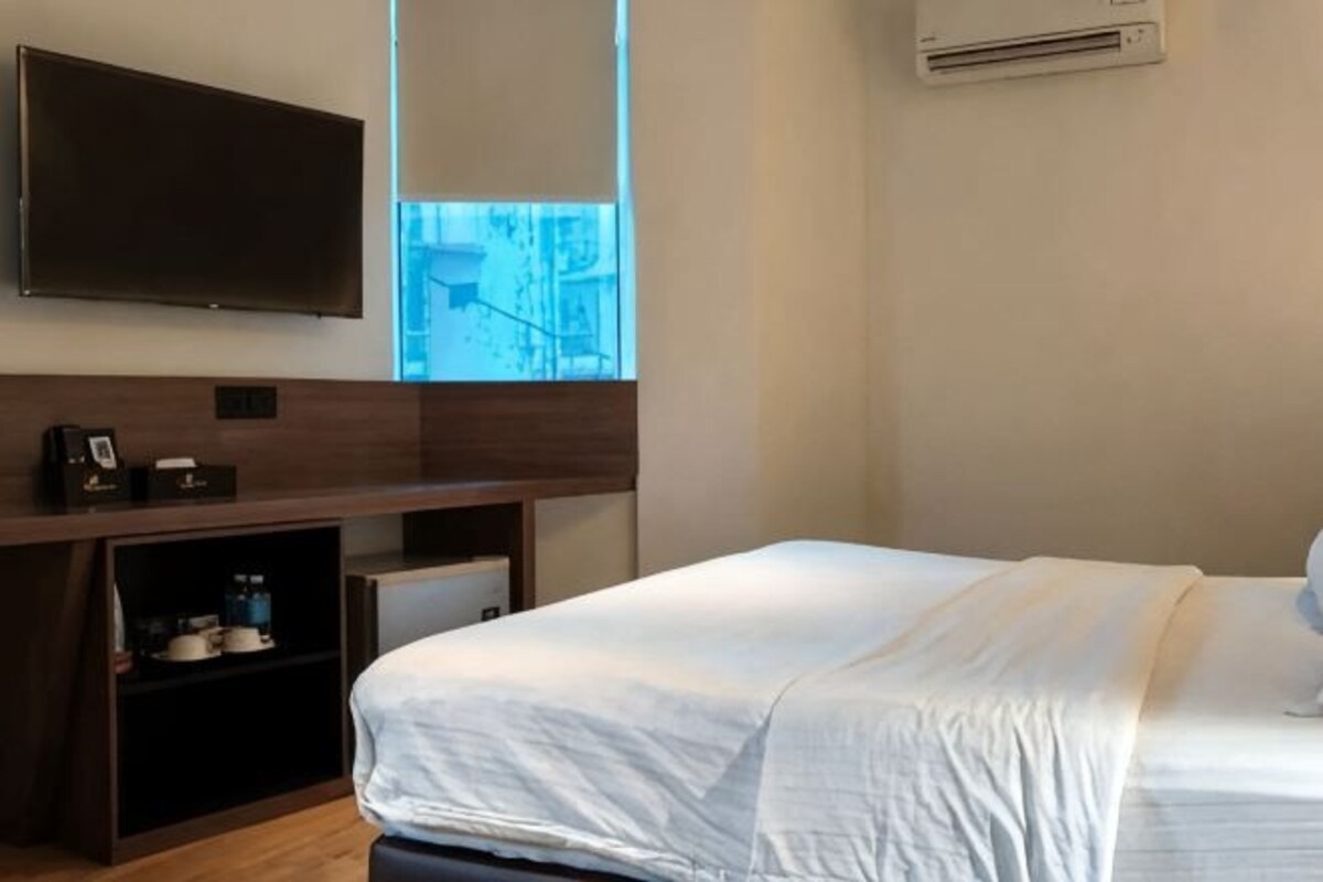 Una habitación de hotel con una cama, un escritorio, un televisor y un aire acondicionado.