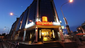 Um hotel chamado "Imperial", com uma entrada notável, uma placa visível da loja 7-Eleven e uma vista clara do céu.