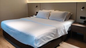 Quarto moderno com cama grande, piso de madeira e mesinhas de cabeceira embutidas.