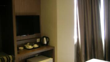 A hotel room with a bed, a TV on a wooden shelf, a small fridge, and a window with curtains.