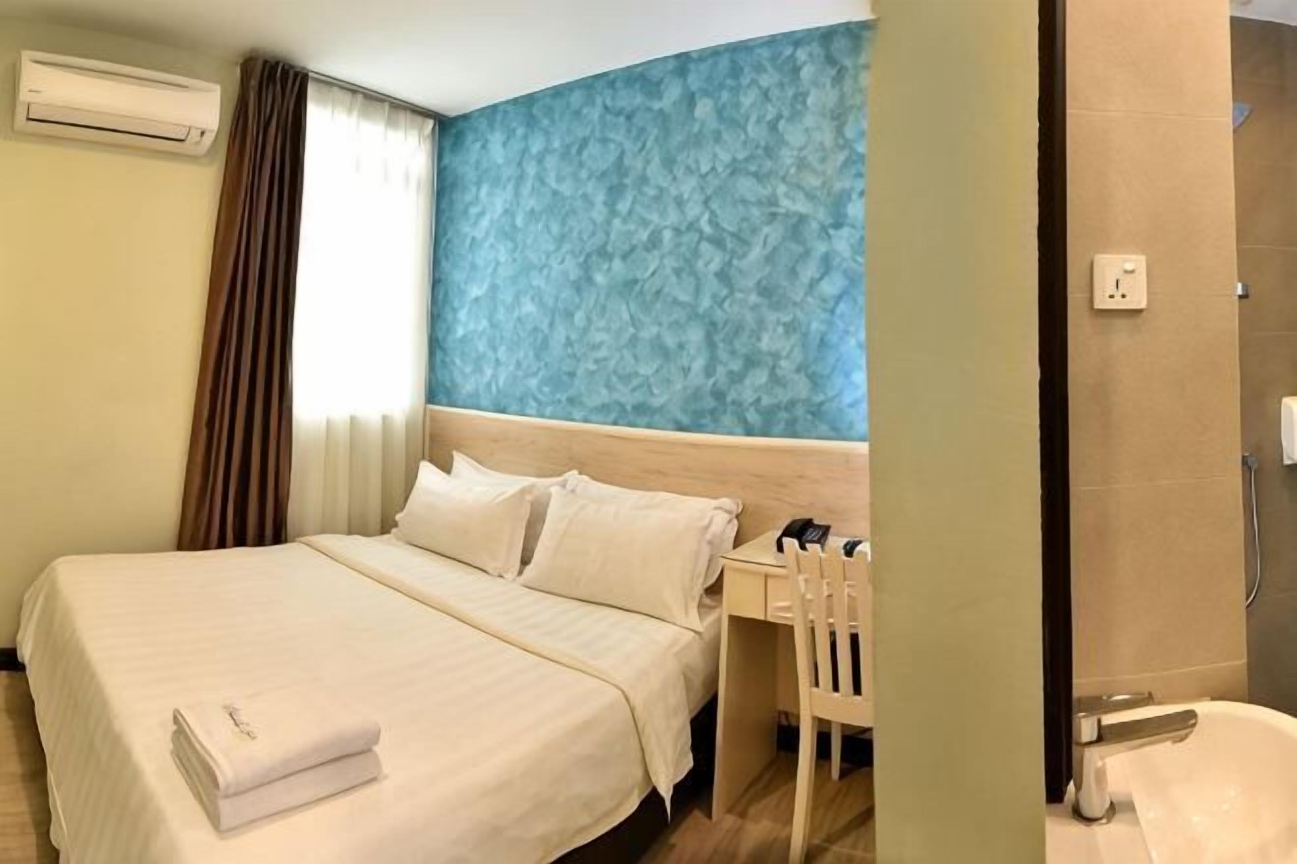 A hotel room with a bed, a desk, a chair, a blue textured wall, and a shower area.