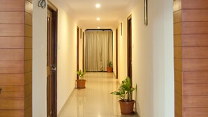 A hallway with wooden paneling, potted plants, and a tiled floor leading to a room with a curtain. - Atlaantic Inn (Bengaluru)