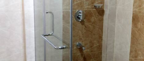 A glass-enclosed shower stall with a handheld showerhead, a handheld showerhead, and a wall-mounted showerhead.