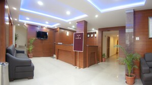 A hotel reception area with a reception desk, a television, clocks, and potted plants. - Atlaantic Inn (Bengaluru)