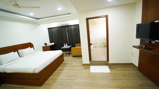 A hotel room with a wooden bed, a TV, a desk, and a chair. - Atlaantic Inn (Bengaluru)