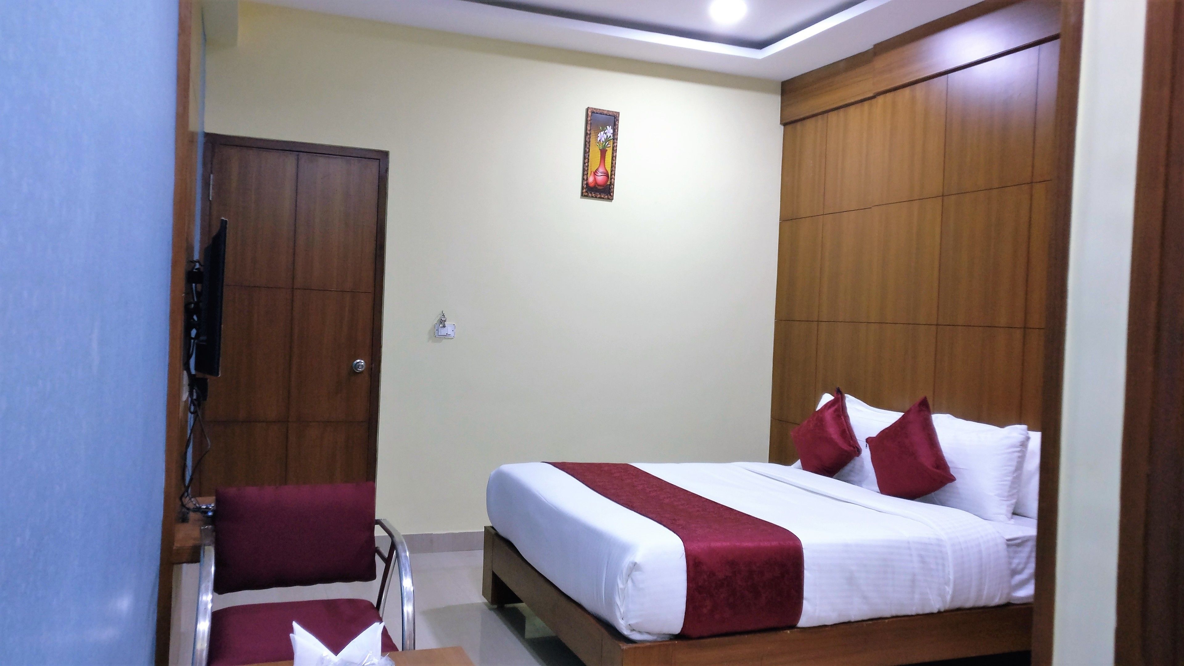 A hotel room with a bed, a desk, a chair, a wardrobe, and a wall-mounted TV.