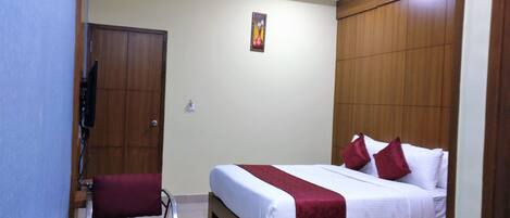 A hotel room with a bed, a desk, a chair, a wardrobe, and a wall-mounted TV.