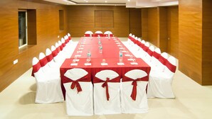 A conference room with a long table, white chairs with red sashes, and wooden paneling on the walls. - Atlaantic Inn (Bengaluru)