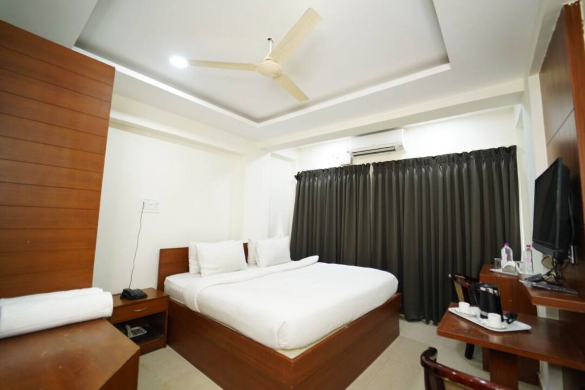 A hotel room with a bed, a desk, a chair, a ceiling fan, and an air conditioning unit.