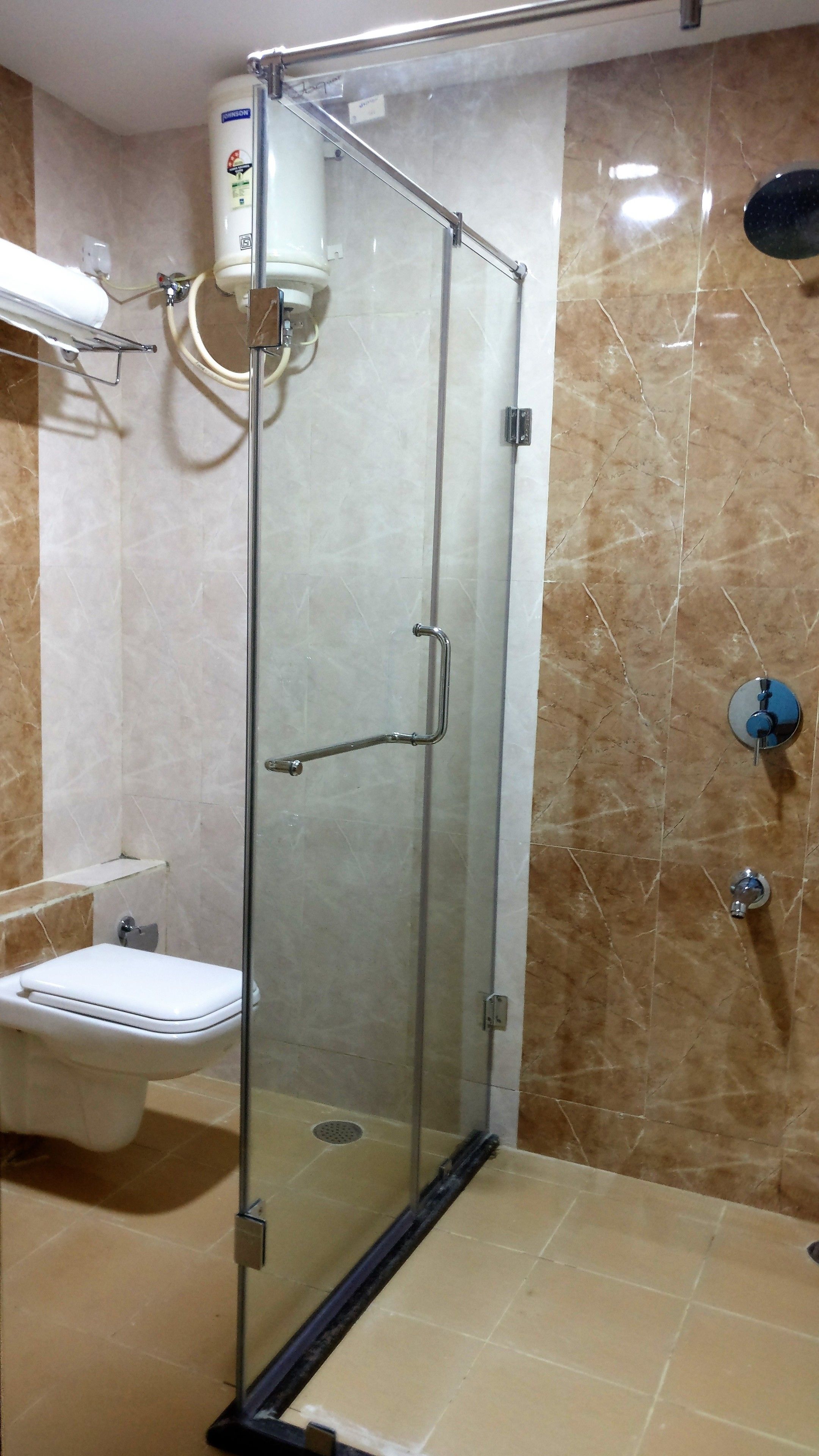 A glass-enclosed shower stall with a white toilet and a towel rack to the left.