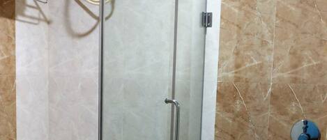 Cabina de ducha con paredes de vidrio, inodoro blanco y un perchero a la izquierda.
