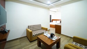 A hotel room with a sofa, a coffee table, a TV, and a bed. - Atlaantic Inn (Bengaluru)