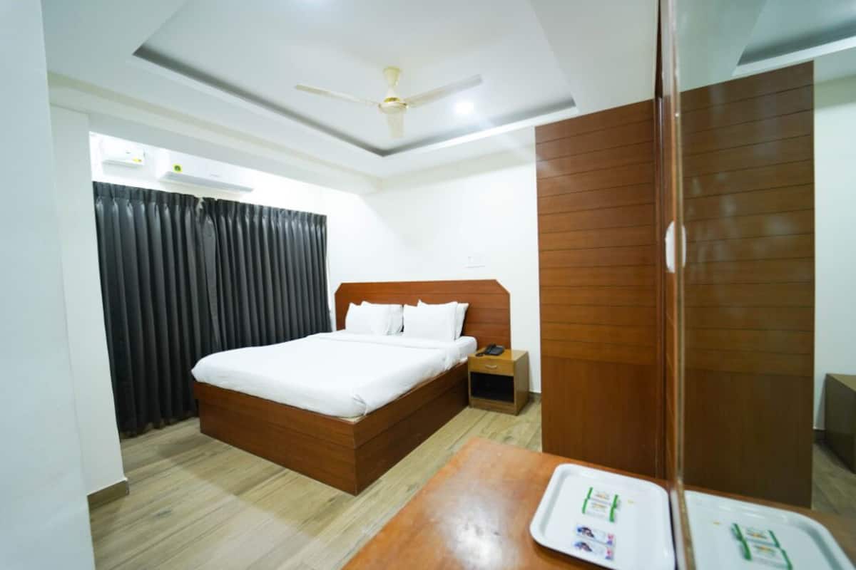 A hotel room with a wooden bed, a nightstand, a desk with a tray, and a wardrobe.